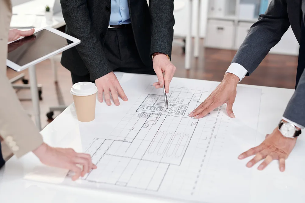 Three people leaning over a large development plan laid on a table