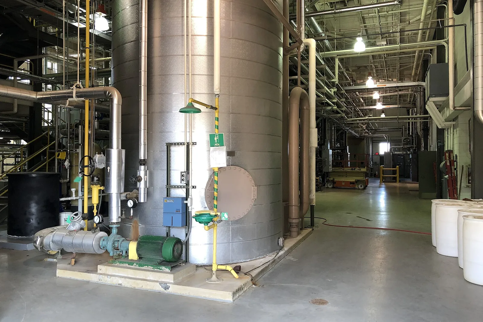 Central boiler plant interior with a large stainless steel tank, insulated pipework and pumps