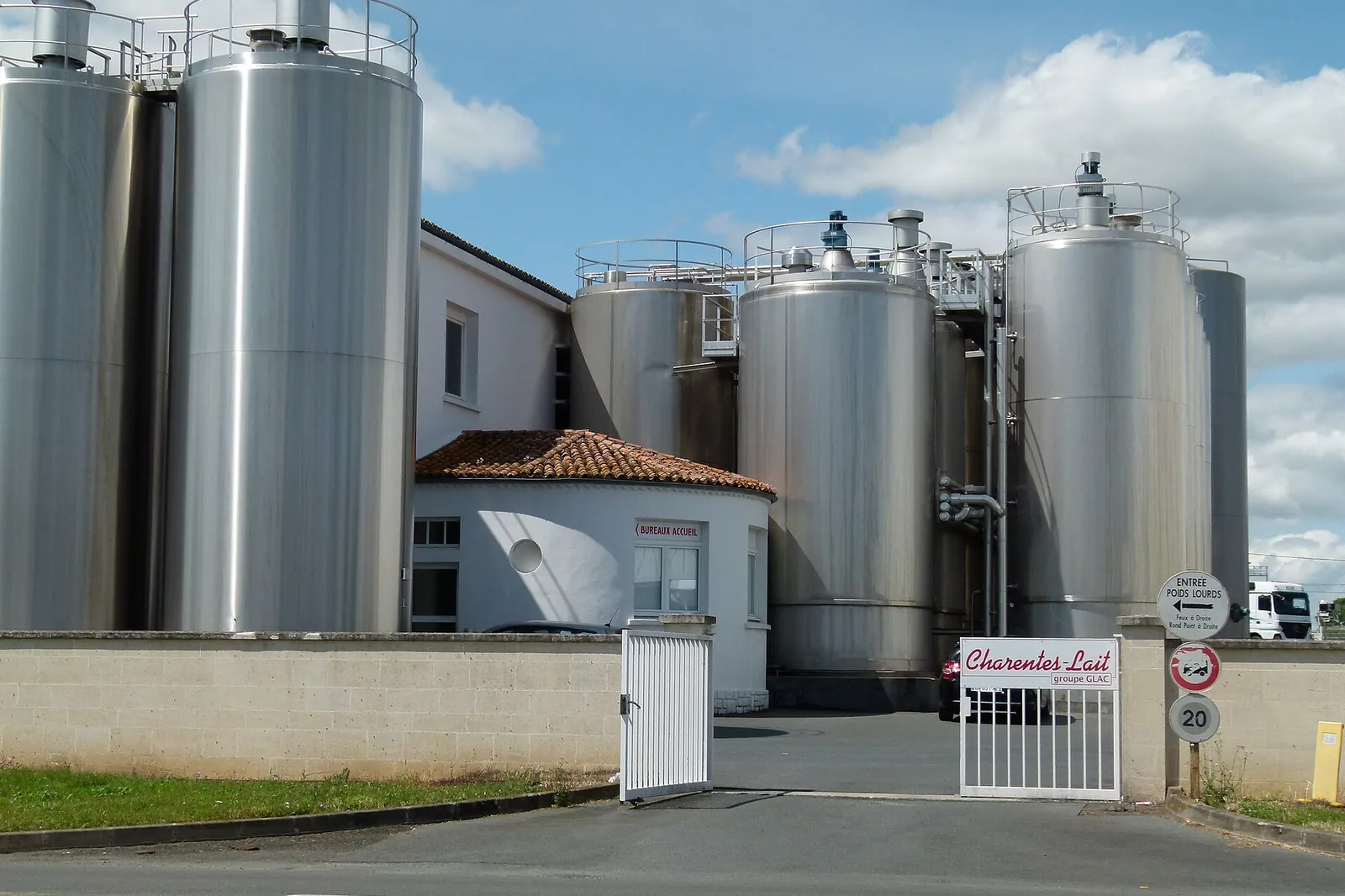 Large stainless steel storage tanks at an industrial dairy behind a gate under a cloudy sky