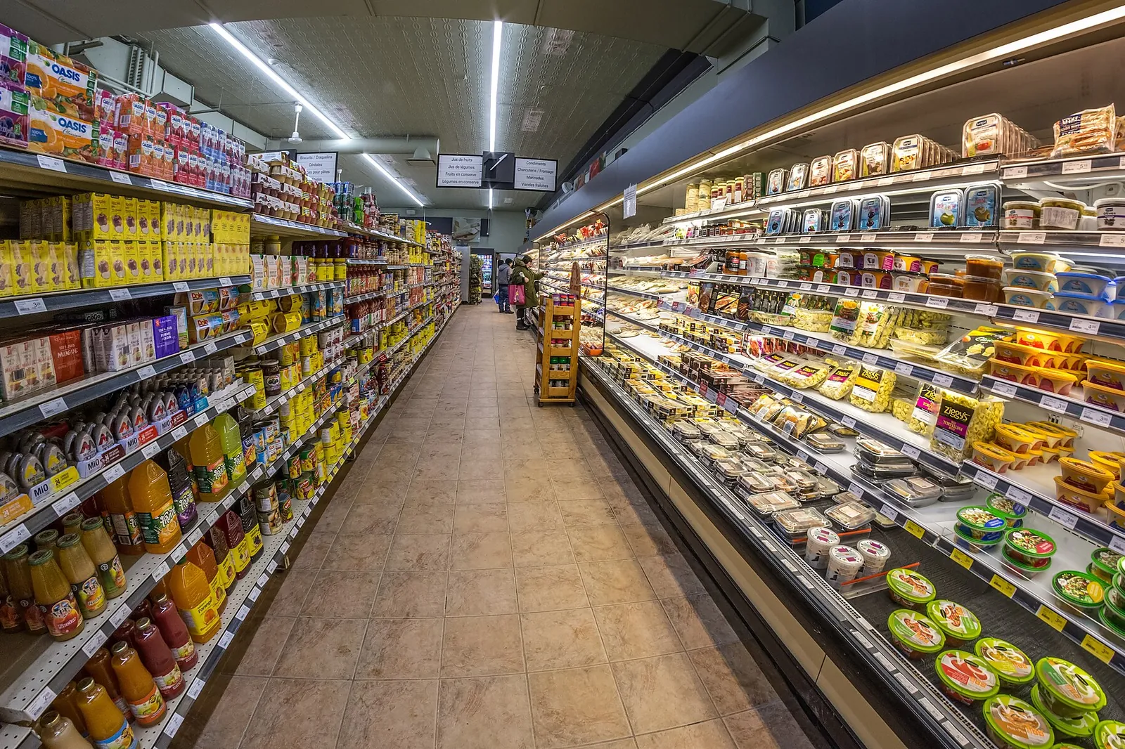 Supermarket aisle lined with open refrigerated cabinets filled with fresh products