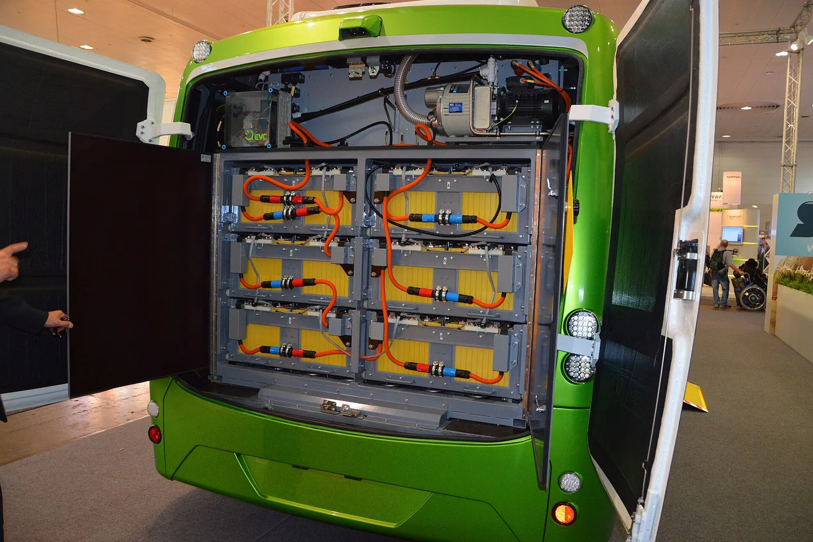 Open rear compartment of an electric bus showing traction battery modules connected by orange cables