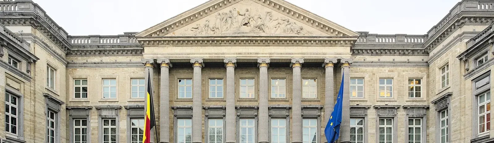 Neoclassical façade of the Palace of the Nation in Brussels, home to the Belgian Federal Parliament, with Belgian and European flags