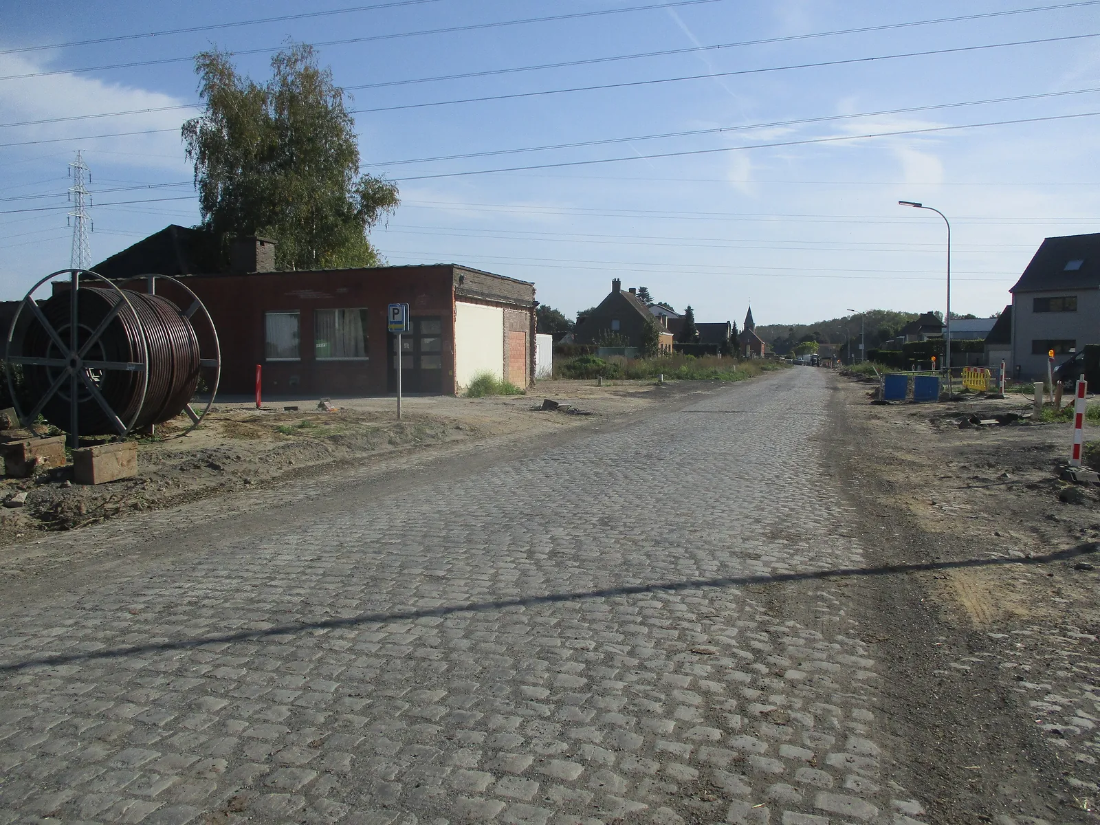 Roadworks on the N409 at Zeveren in East Flanders: exposed cobbled carriageway and a cable reel on the verge
