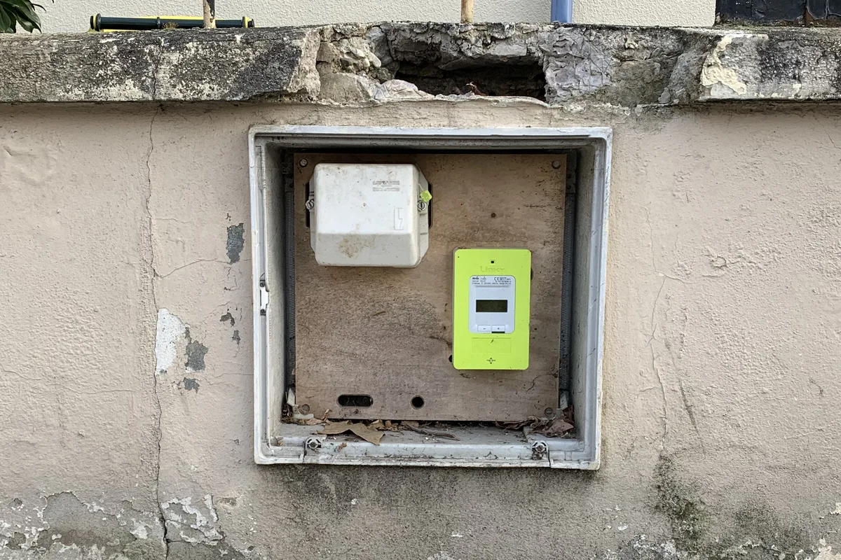 Green Linky electricity meter and white box in an open cabinet set into a street wall in Lyon