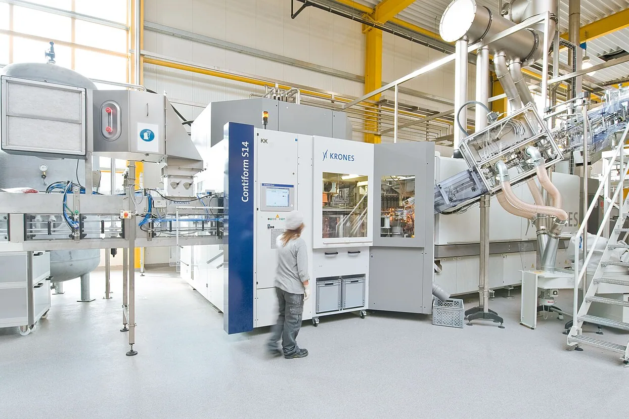 PET bottle blow-moulding machine in a bright workshop, with an operator in front of the machine