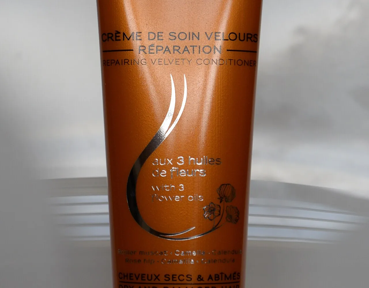 Orange tube of Melvita hair-care cream bearing the claim "with 3 flower oils" in French and drawn flowers