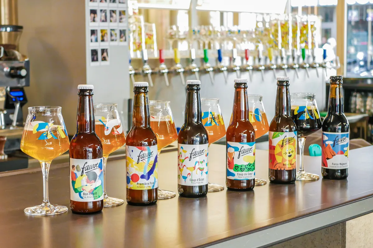 Craft beer bottles with colourful labels lined up on the counter of a Paris brewery, in front of the taps