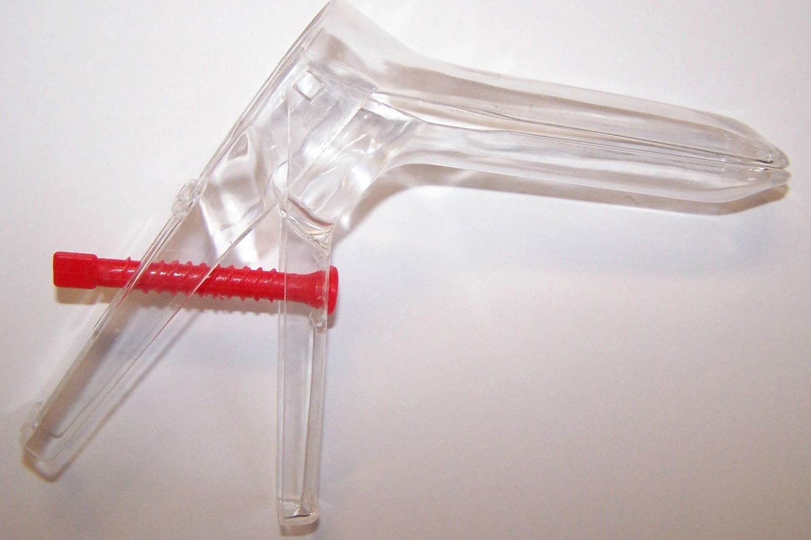 Transparent plastic single-use vaginal speculum with its red adjustment screw, on a white background
