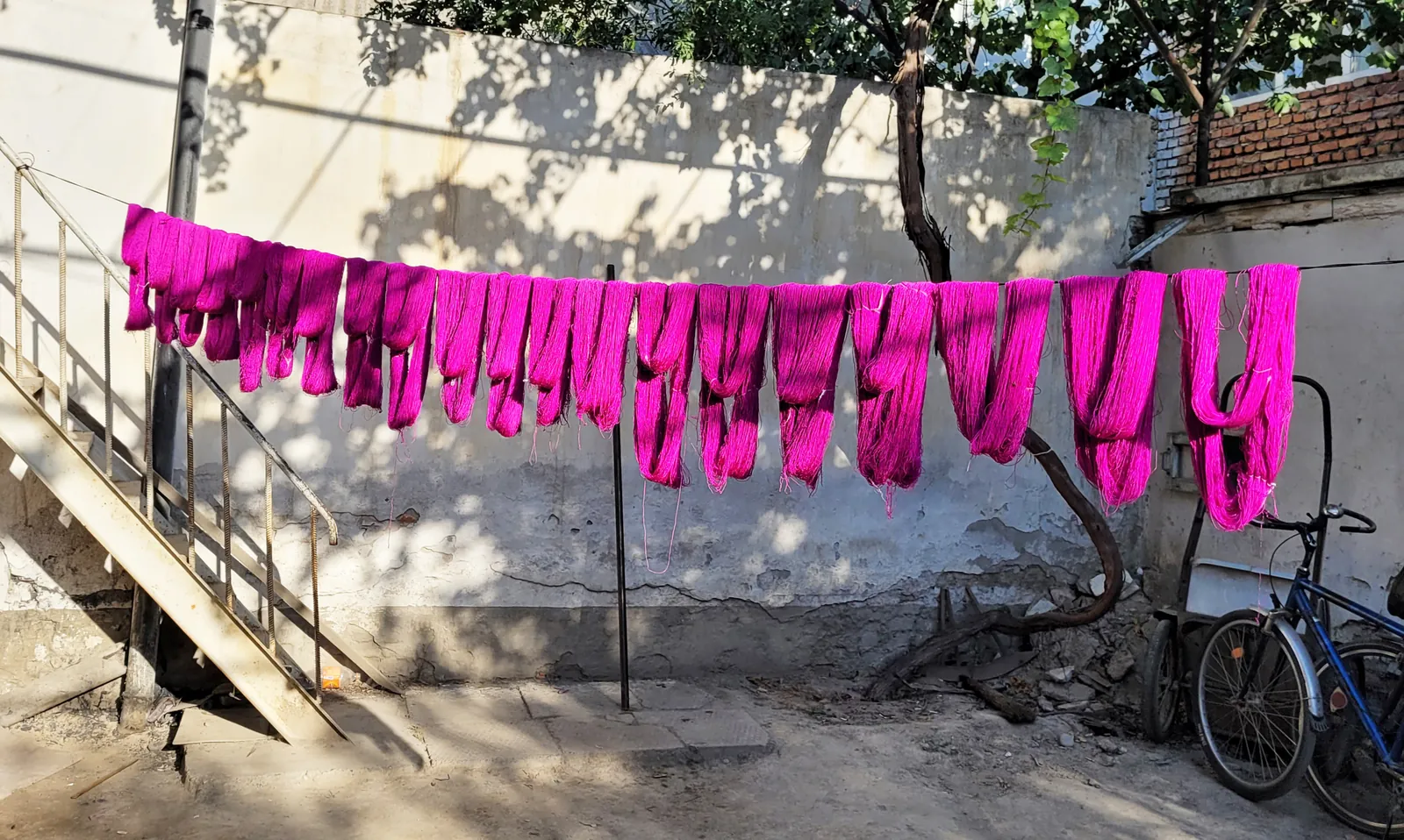Magenta-dyed silk skeins drying on a line in a workshop courtyard