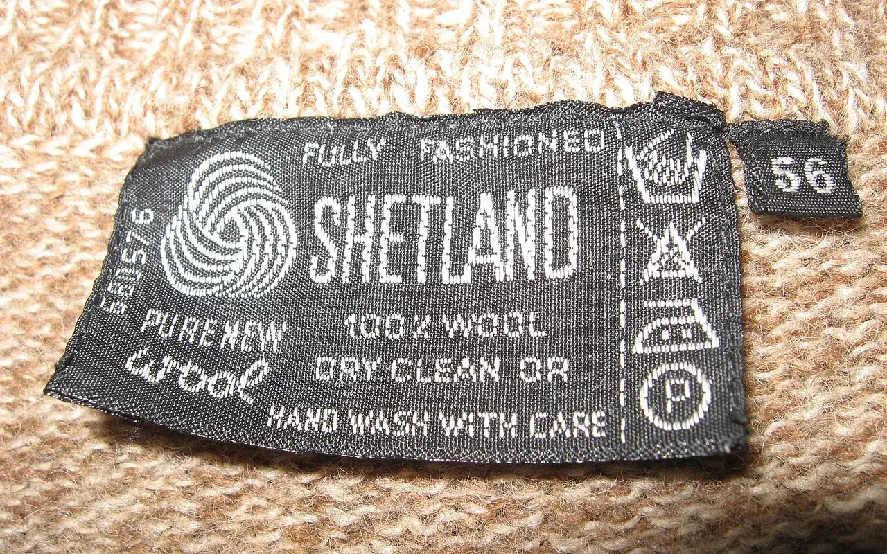 Black label sewn into a beige jumper: Shetland, 100% wool, pure new wool, with care symbols and size 56