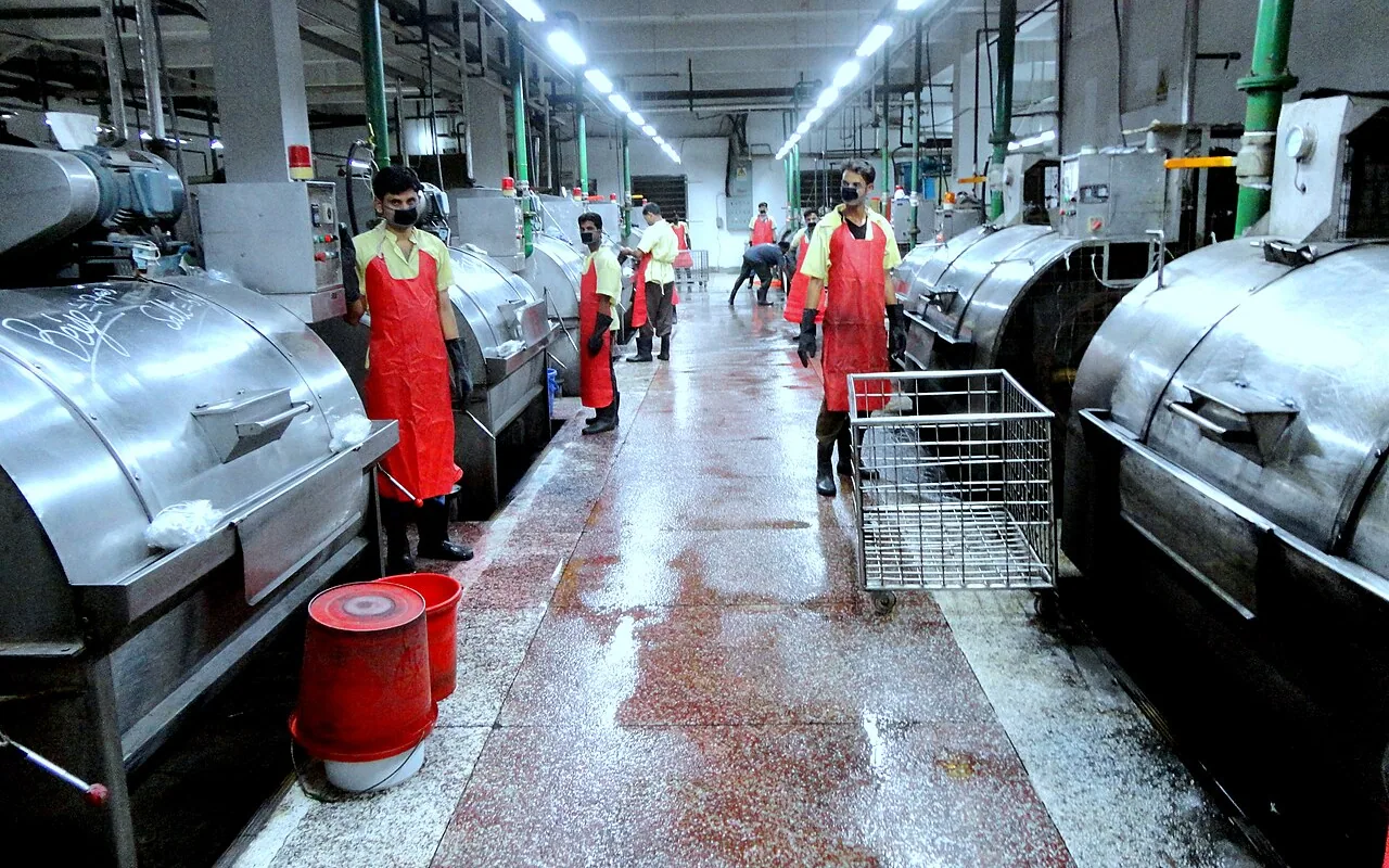 Central aisle of a jeans laundry lined with stainless steel industrial washing machines, with workers in red aprons