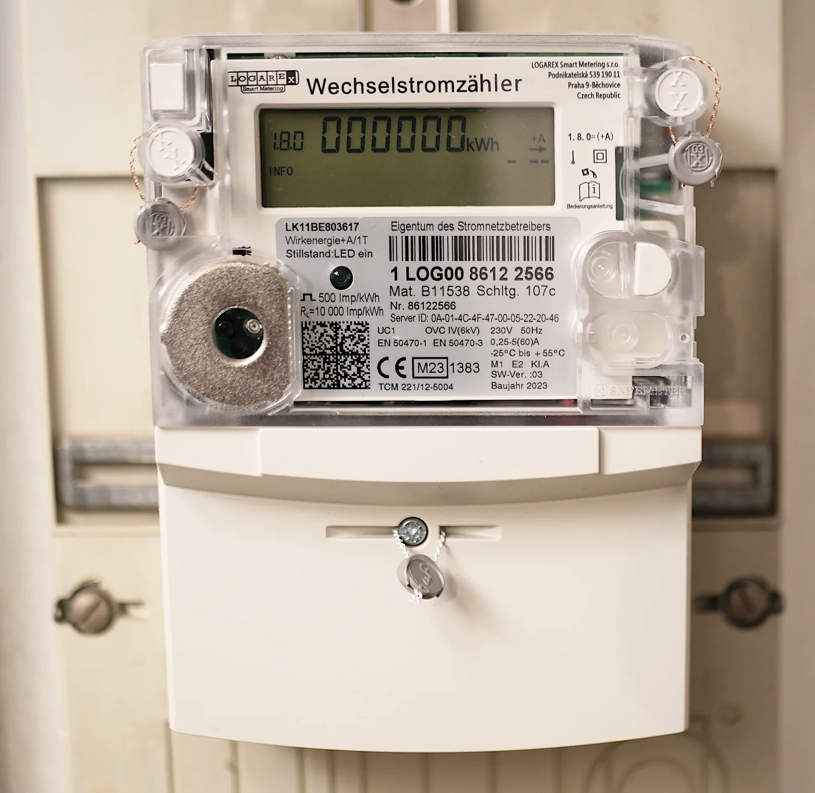 Grey smart electricity meter with its digital display, QR code and technical markings, installed in a home