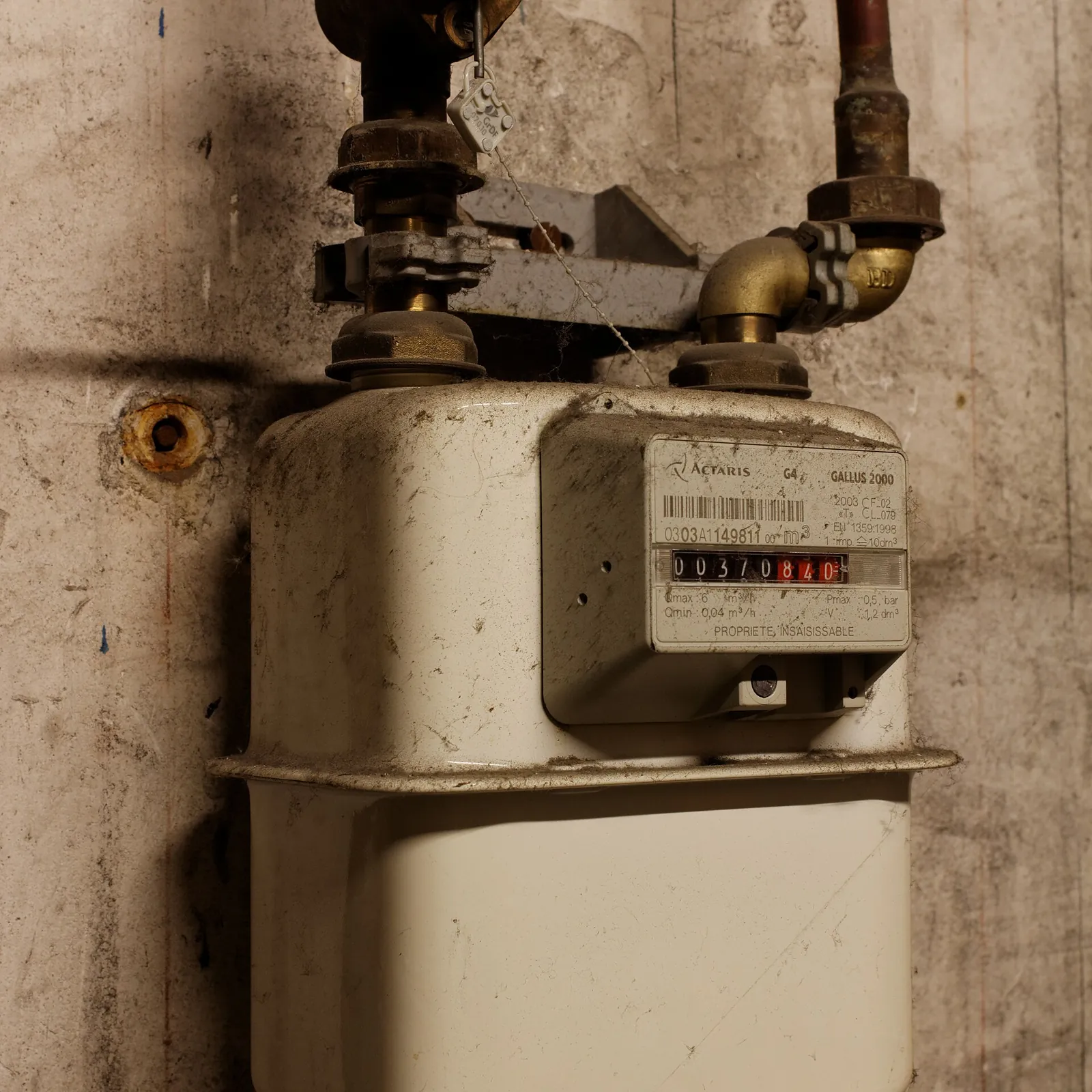 Old gas meter mounted on a basement wall, with its pipes and valve
