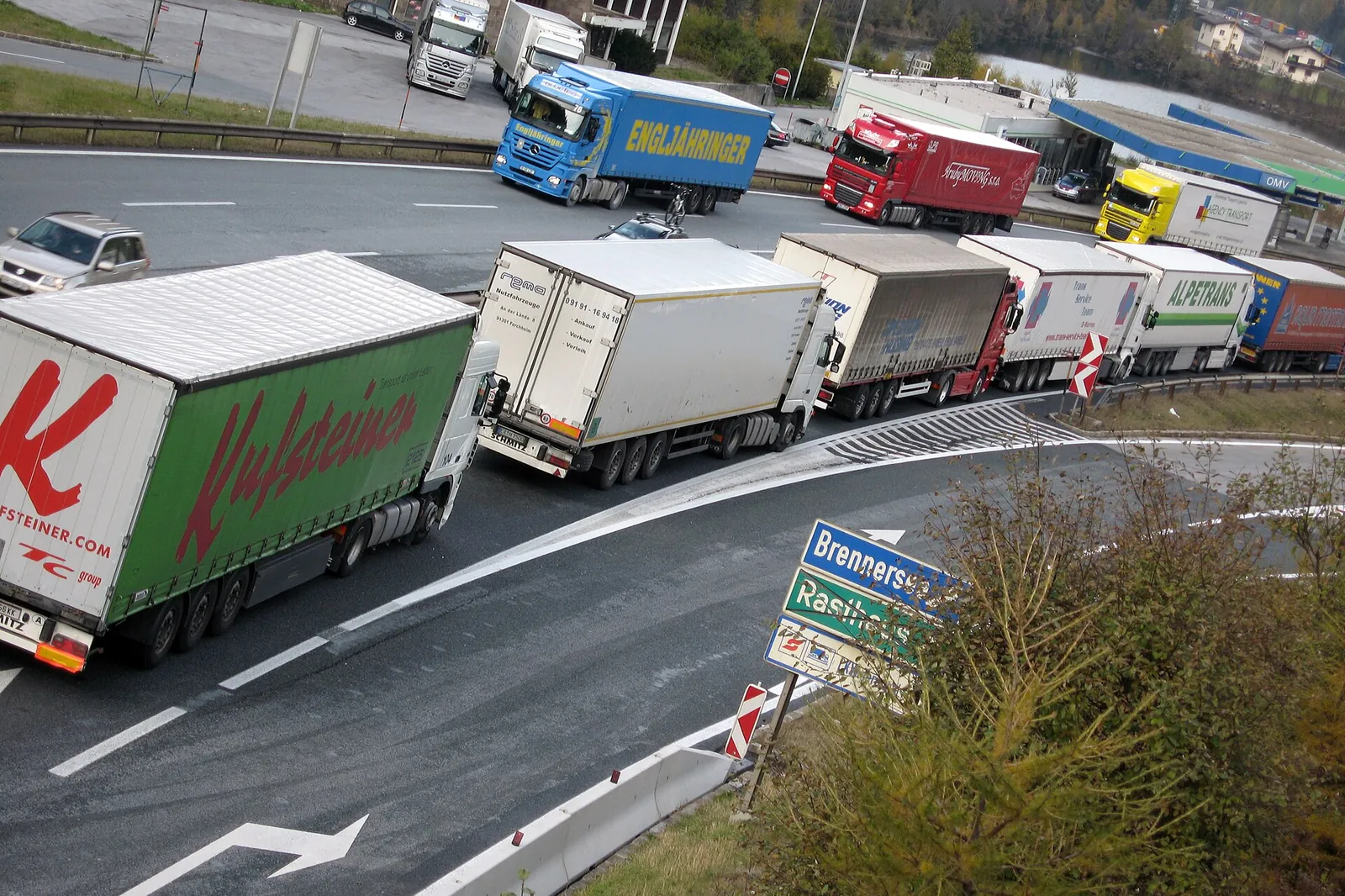 Queue of stationary heavy goods vehicles on a curved motorway approaching a toll plaza