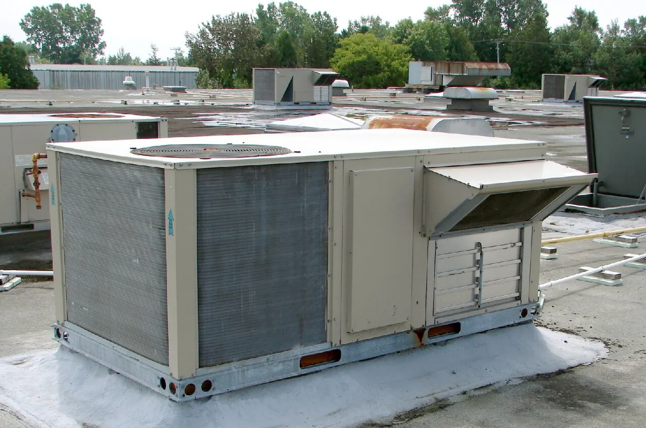 A heating and air-conditioning unit placed on the flat roof of a building, other units visible in the background