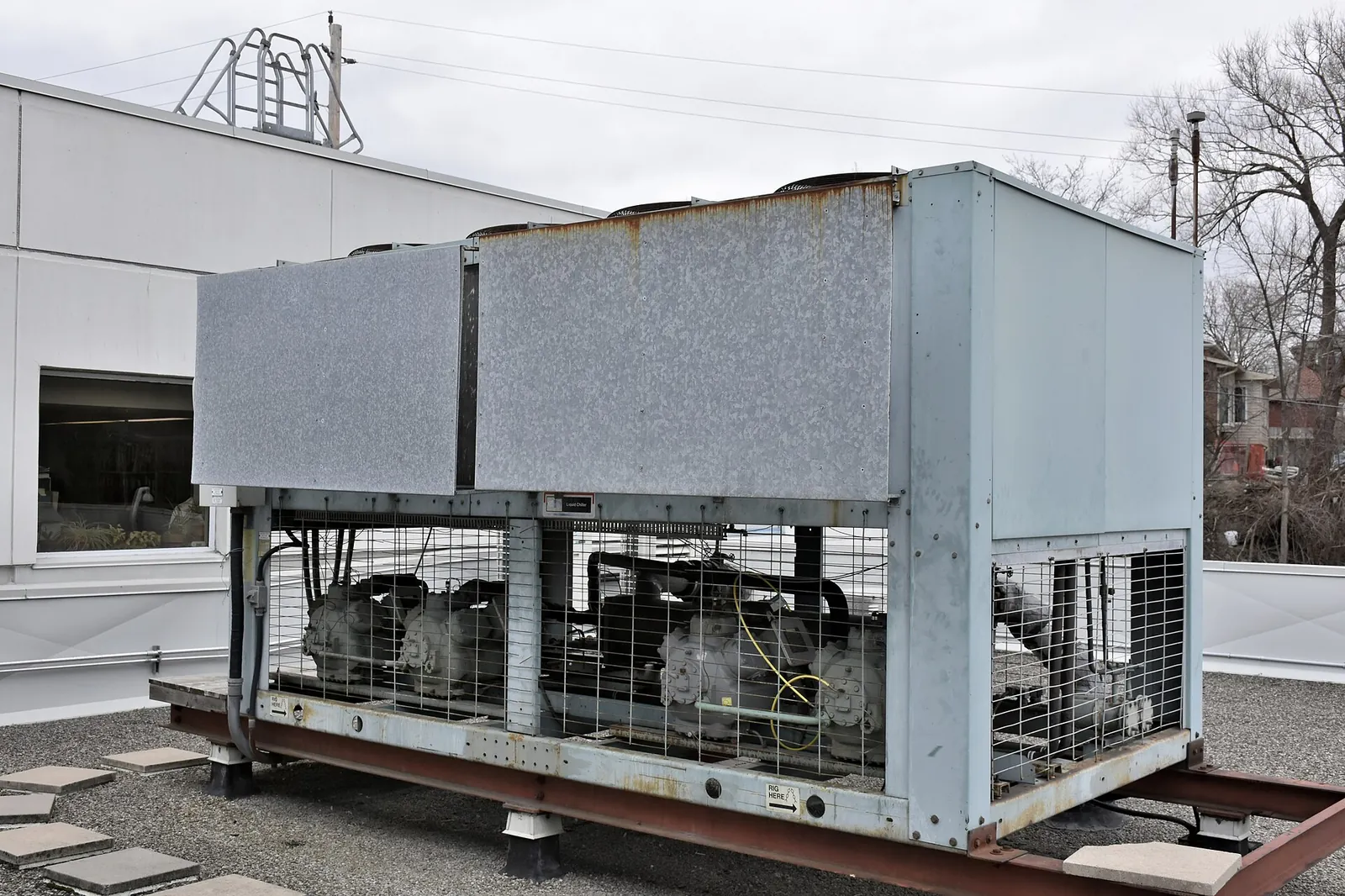 Air-cooled chiller on a building's roof, with compressors visible behind a grille