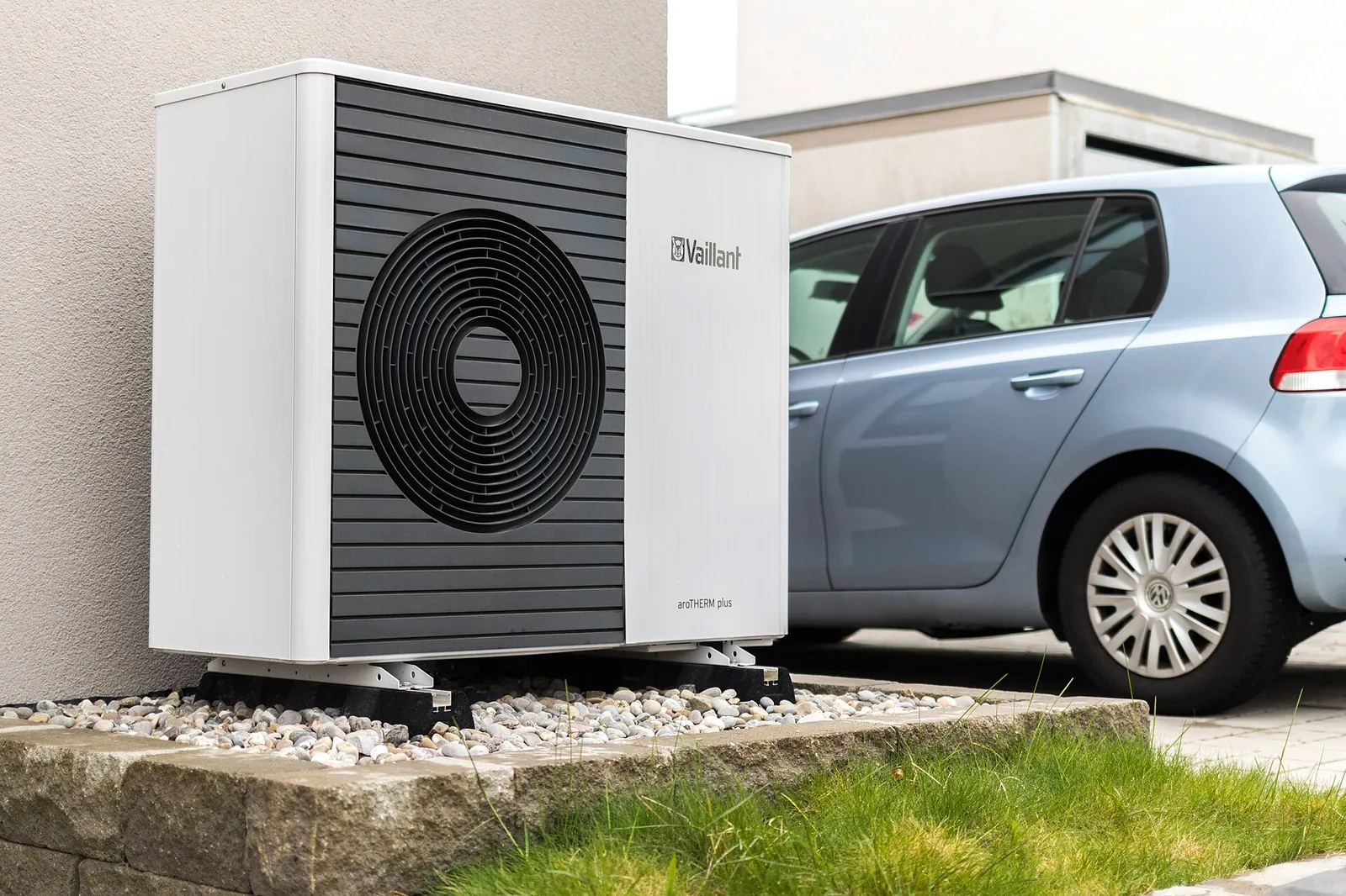 White and anthracite outdoor air-to-water heat pump unit standing on pebbles in front of a house