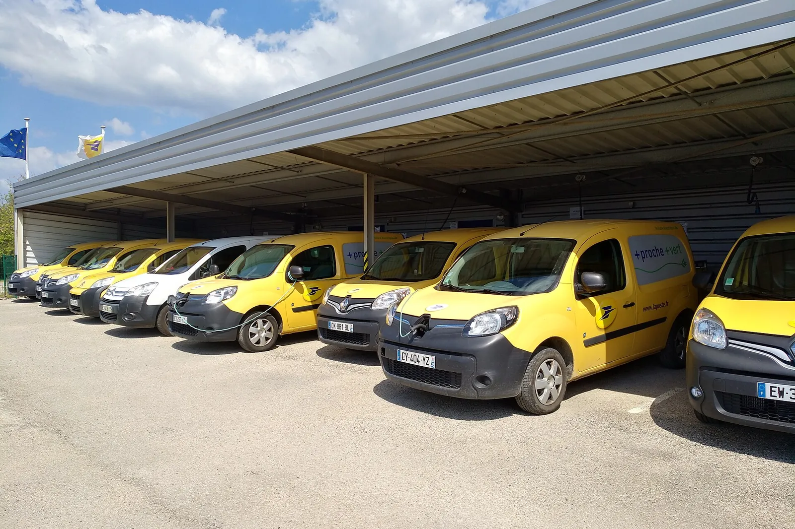 Yellow La Poste commercial vehicles parked in a row under a depot canopy in Clairvaux-les-Lacs, Jura