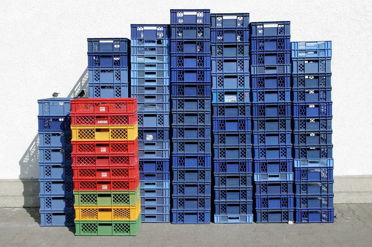 Stacks of blue, red, yellow and green plastic shipping crates leaning against a white wall in a recycling plant