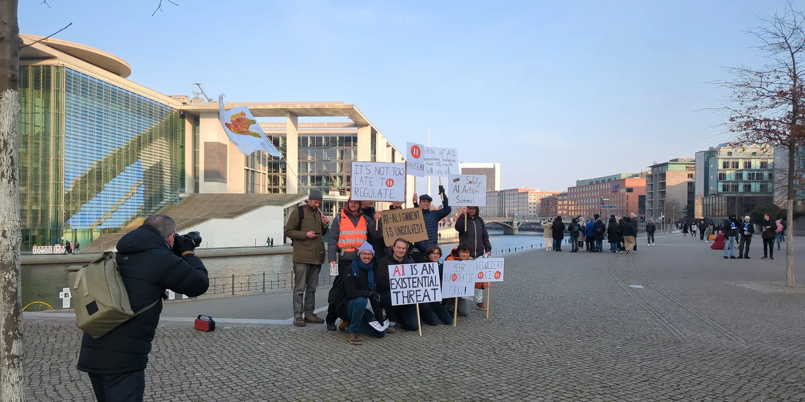 About ten protesters hold signs calling for AI to be regulated, beside the water in Berlin