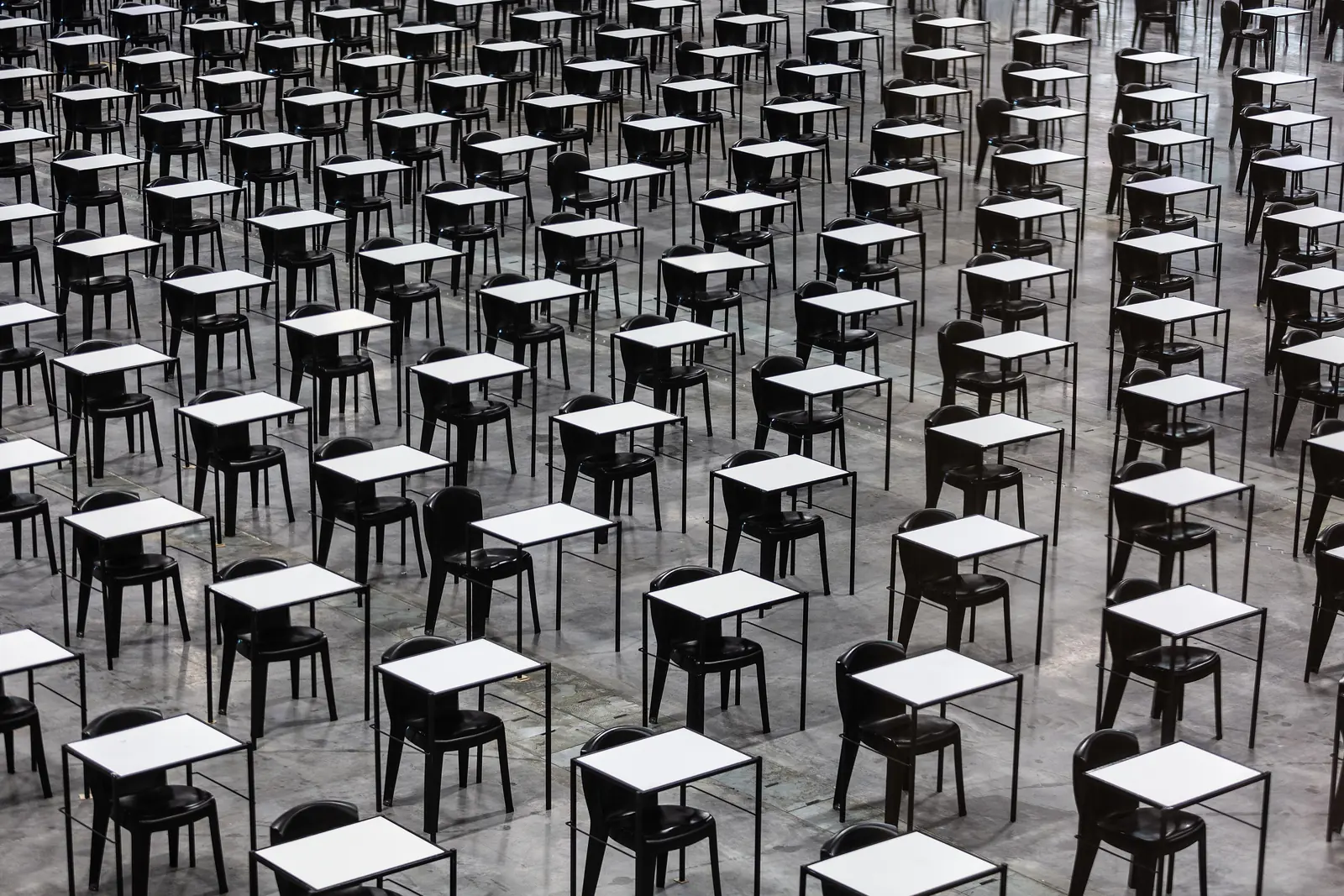More than a hundred small exam desks and empty chairs, lined up diagonally and seen from above