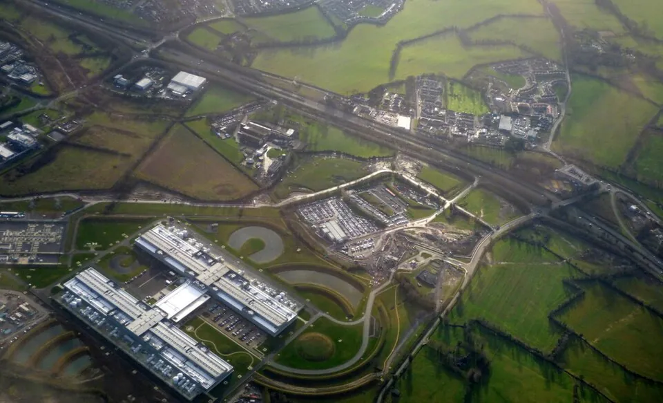 Aerial view of a data centre: 2 long buildings with pale roofs in the middle of hedged Irish farmland, alongside a motorway