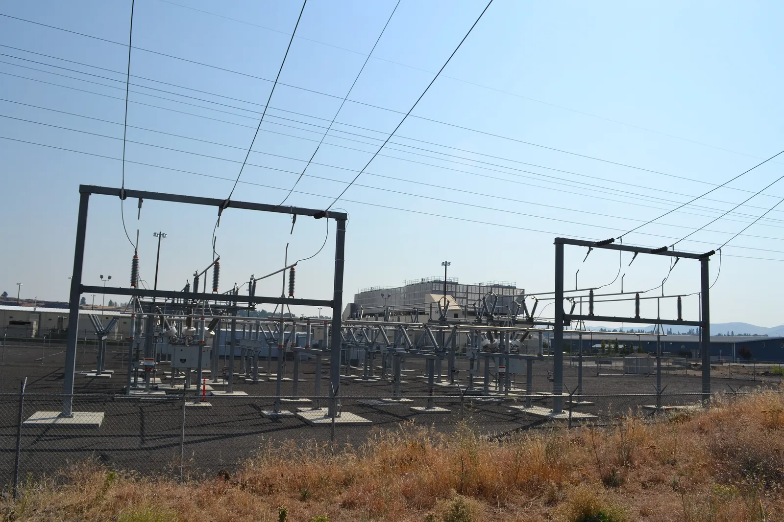 An electrical substation in the foreground, with its gantries and lines, in front of the buildings of a Google data centre