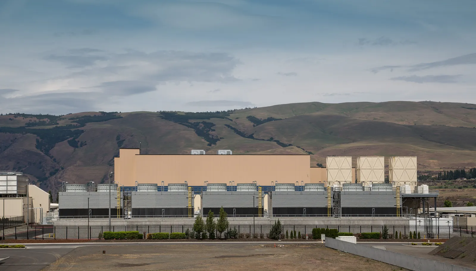 A Google data centre: a long beige building fronted by a row of cooling towers, in front of hills