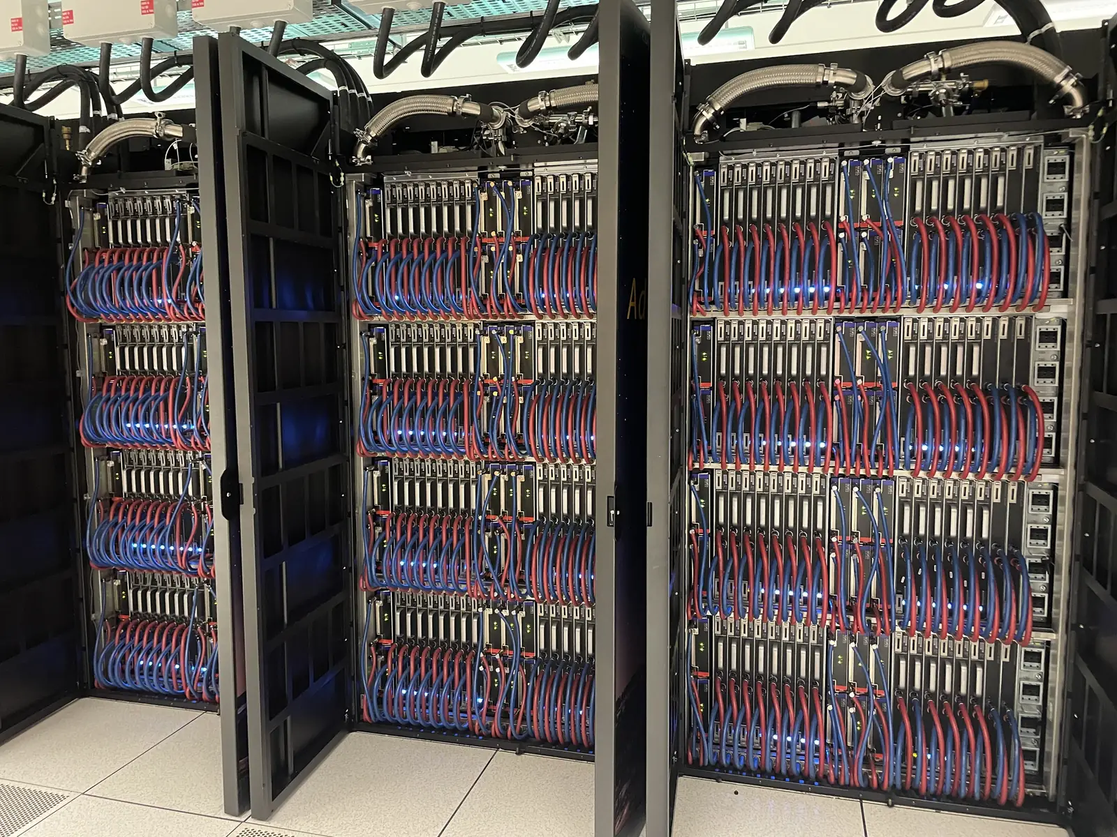3 open racks of a supercomputer, with their compute blades and the red and blue pipes of the liquid cooling