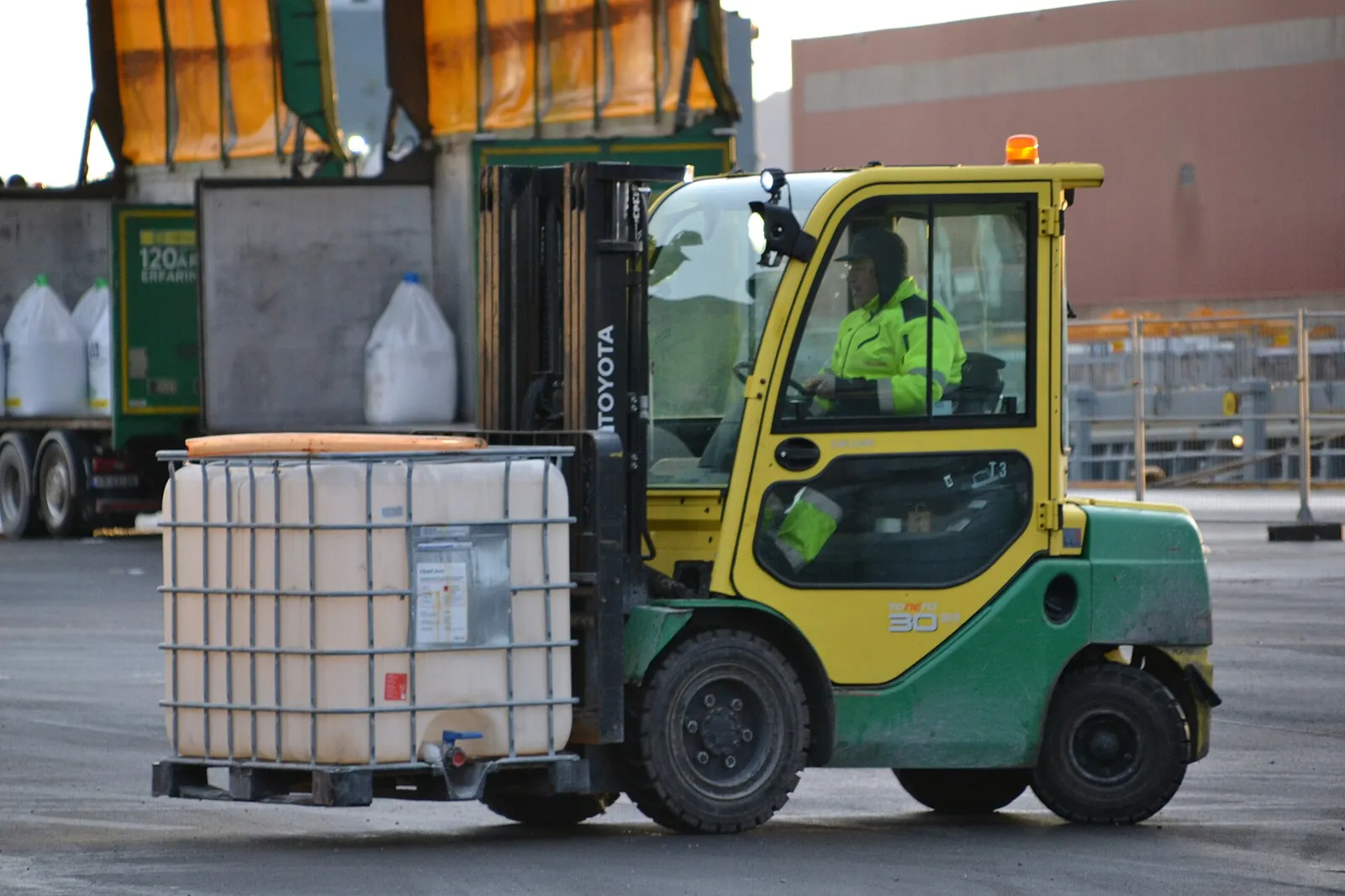 Forklift truck moving a white plastic intermediate bulk container (IBC) in its metal cage, on a pallet, on a harbour quay