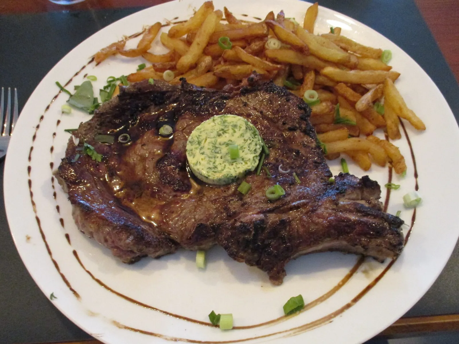 A grilled rib of beef with herb butter and chips on a white plate
