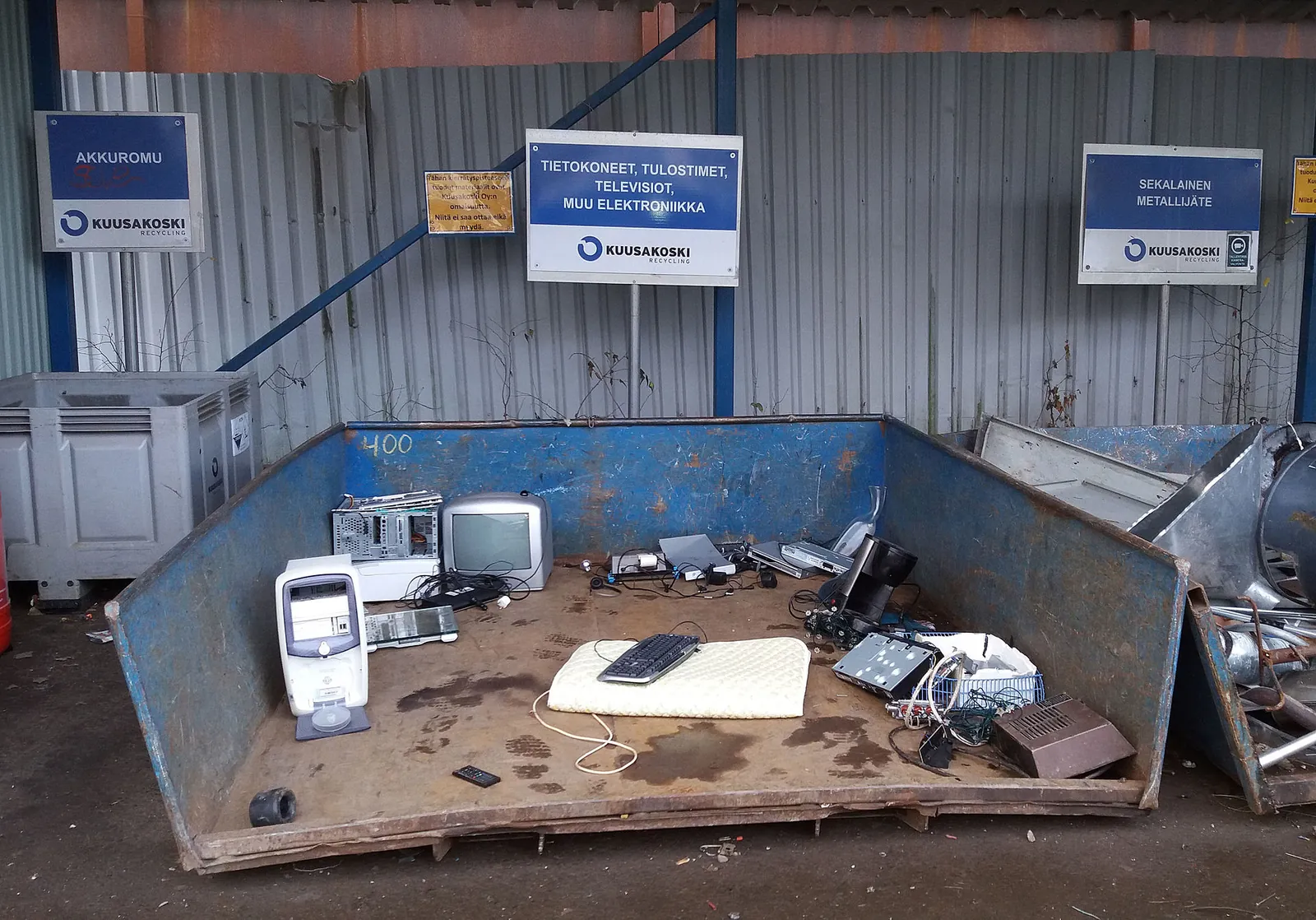 A blue skip full of computers, a television and keyboards, under a sheet-metal canopy