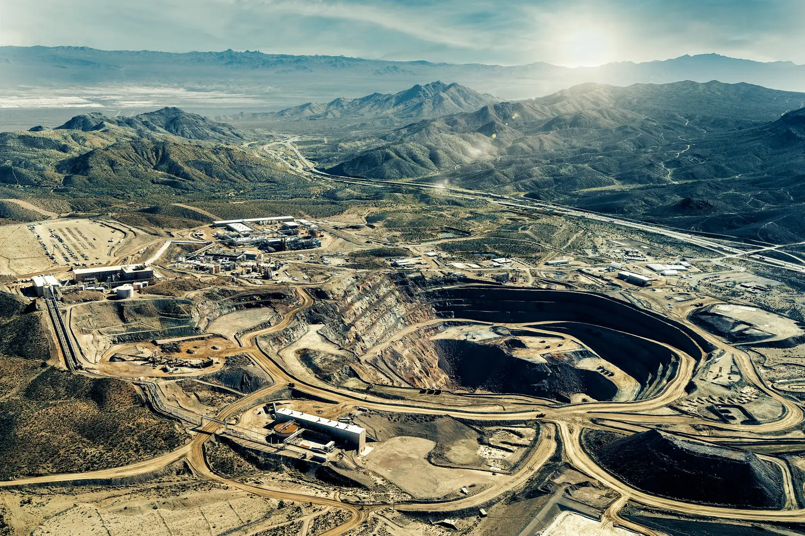 Aerial view of a terraced open-pit mine and its processing plant, in a desert mountain landscape