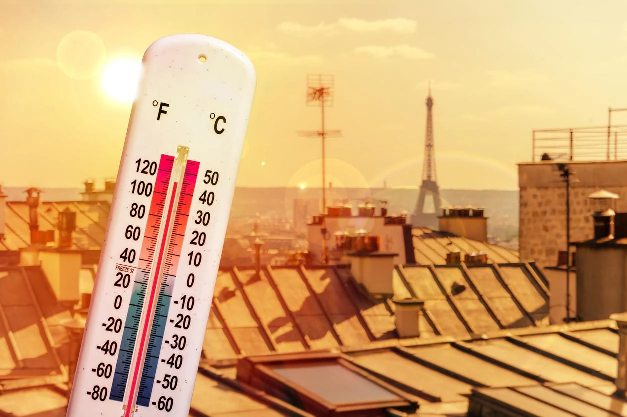 Thermometer in front of the rooftops of Paris under a heatwave sun, with the Eiffel Tower in the heat haze