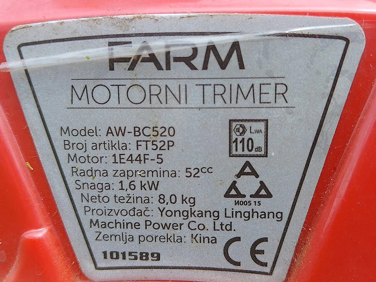 Red and silver rating plate of a petrol brush cutter, showing model, serial number, power, country of origin and CE marking