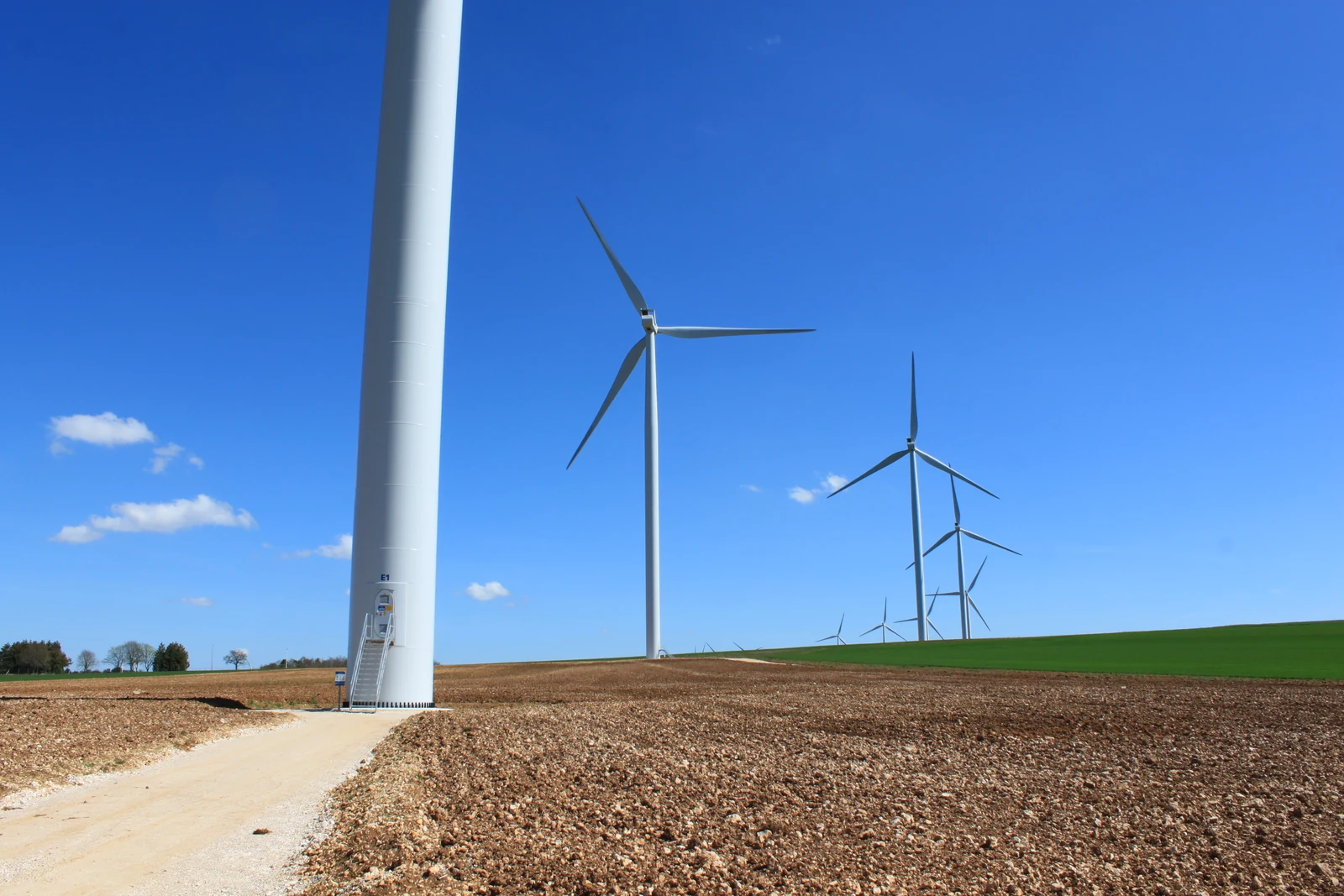 Wind turbines of the Chitry-Quenne wind farm in a ploughed field under a blue sky, with the mast of a turbine in the foreground