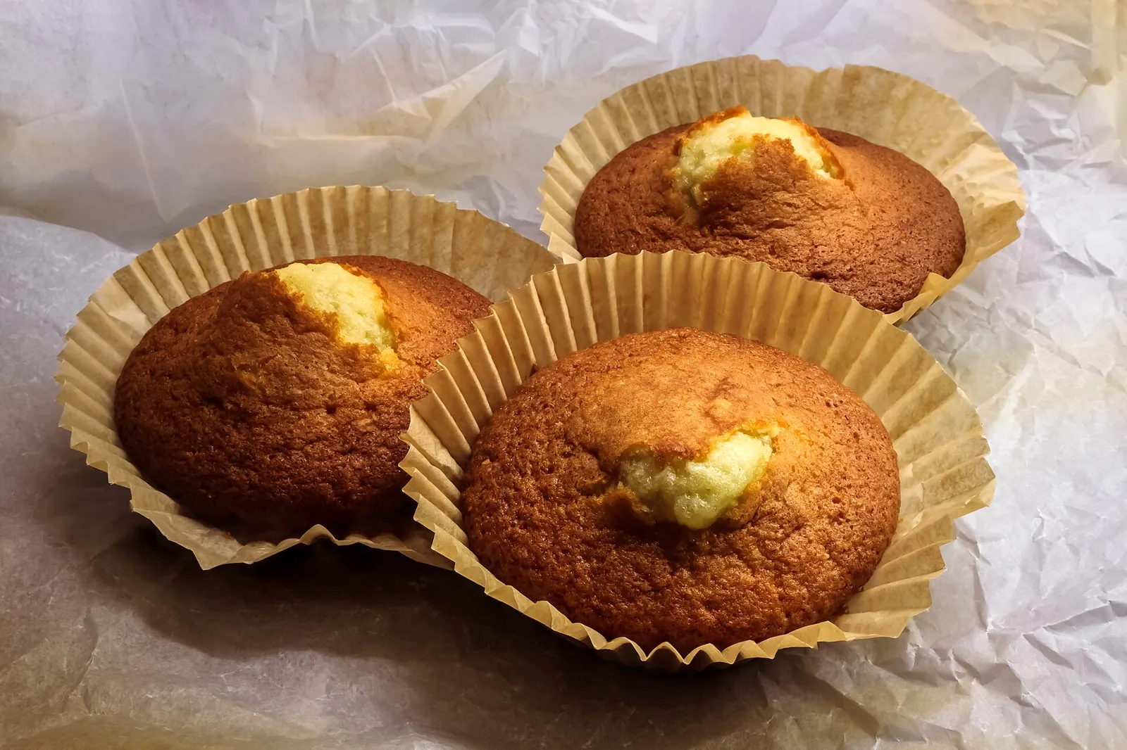 Vanilla muffins in pleated paper cases, placed on a sheet of paper