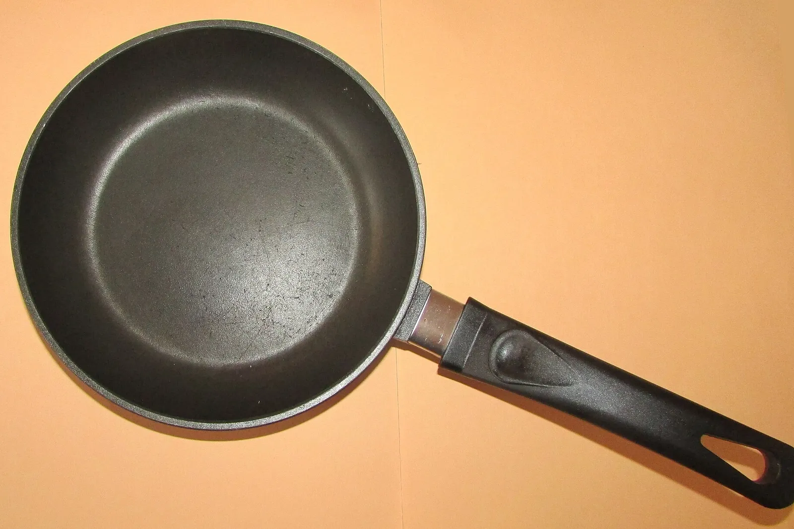 Black non-stick PTFE-coated frying pan seen from above, on an orange background