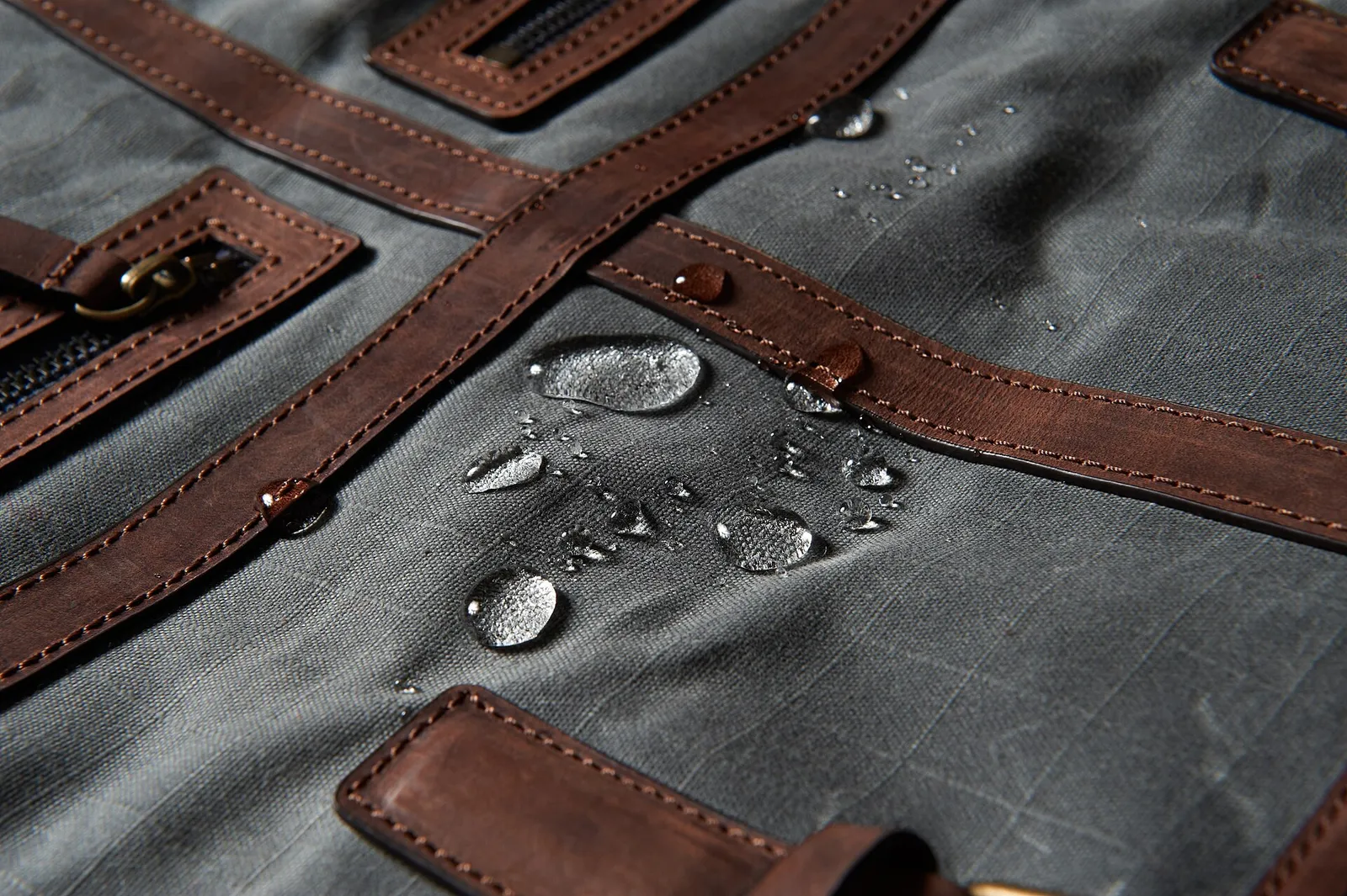 Water droplets beading on grey waxed cotton canvas edged with leather straps