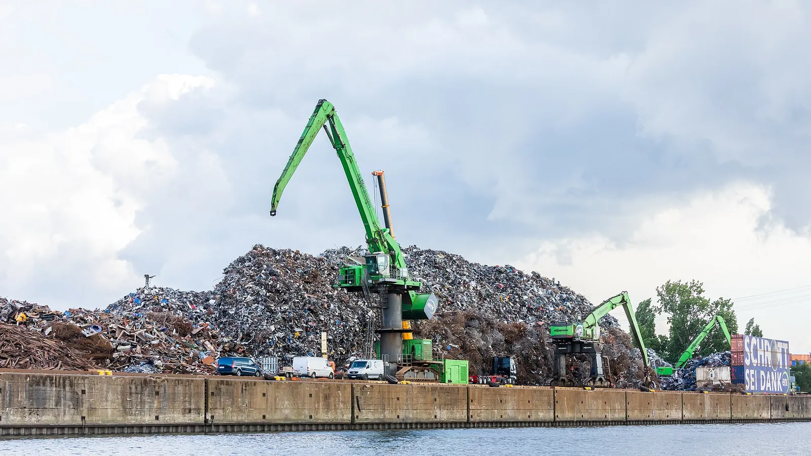 Heap of scrap metal on a metal recycling quay in Hamburg, with several green handling cranes