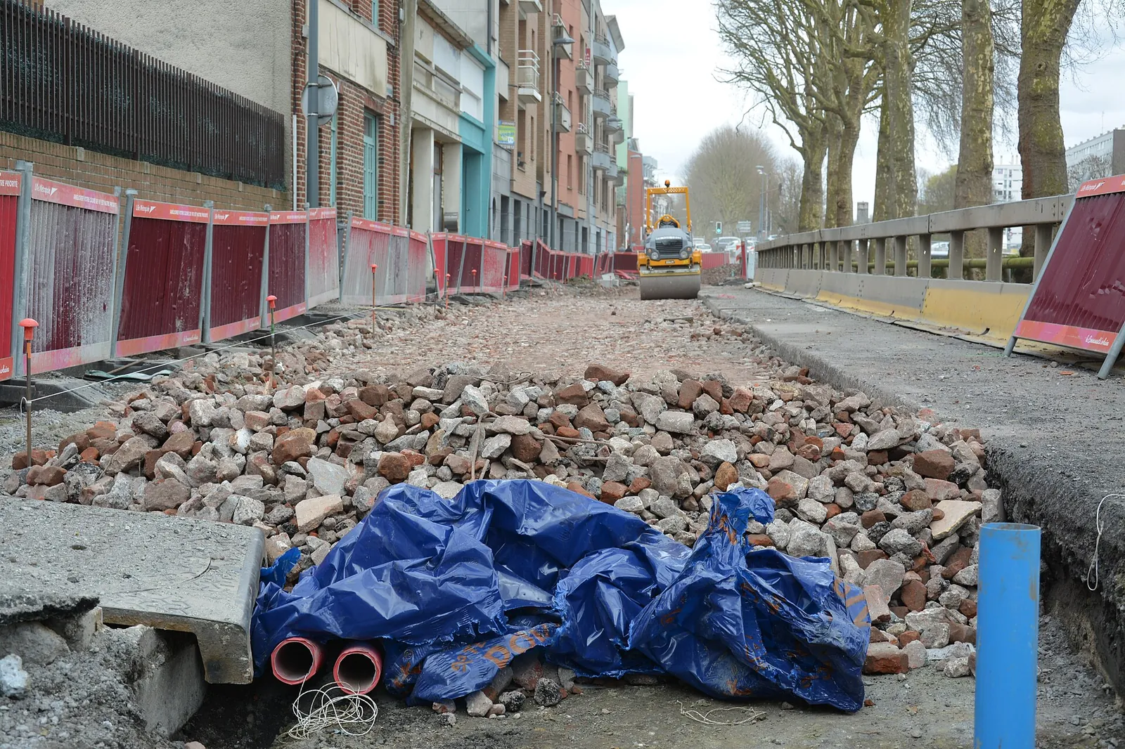 Piles of crushed brick rubble spread over a road under construction in Lille, between site barriers and brick façades