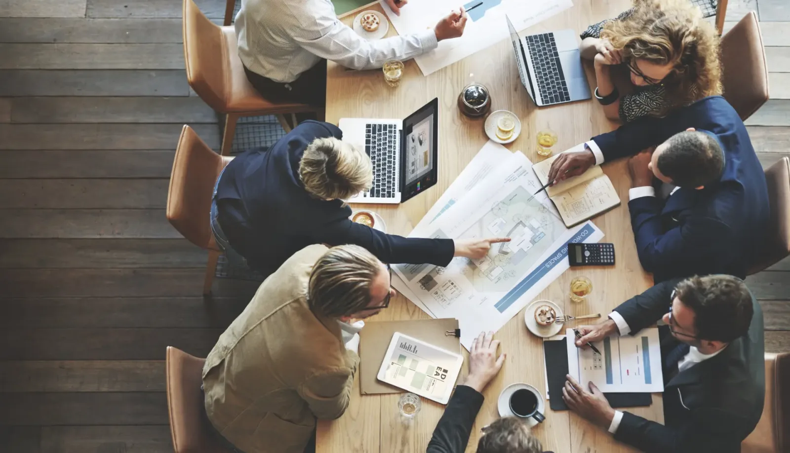 Overhead view of a meeting around a table with plans, computers and documents