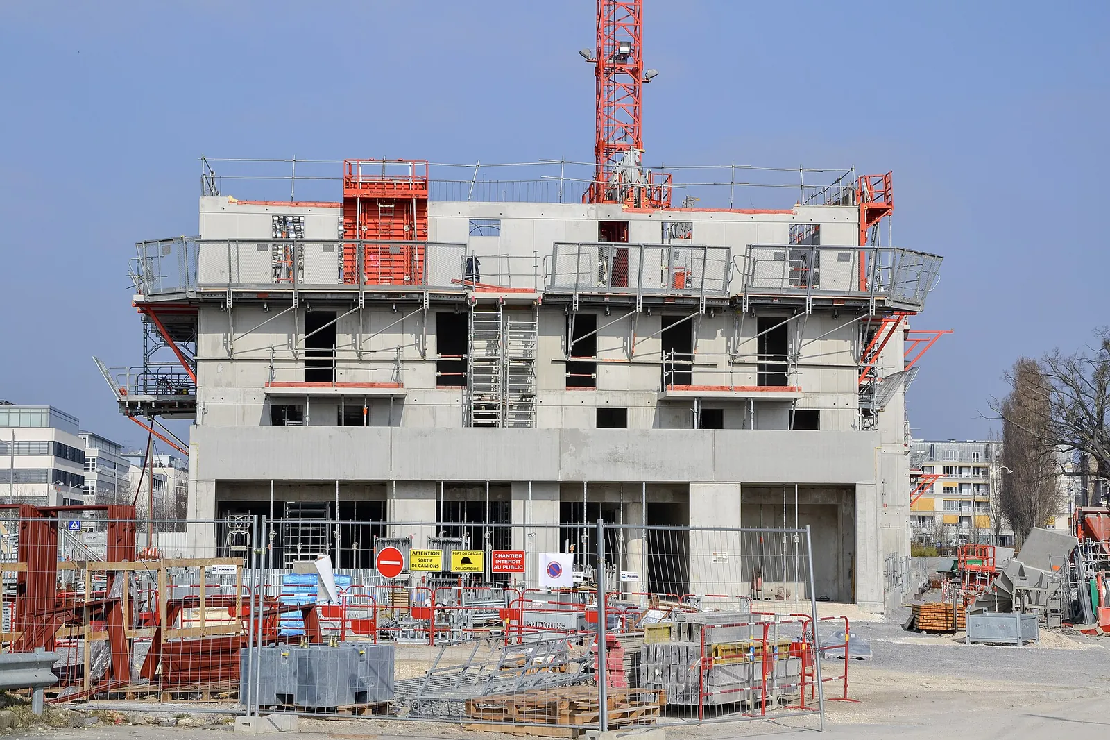 Concrete apartment building under construction, with crane and red safety scaffolding
