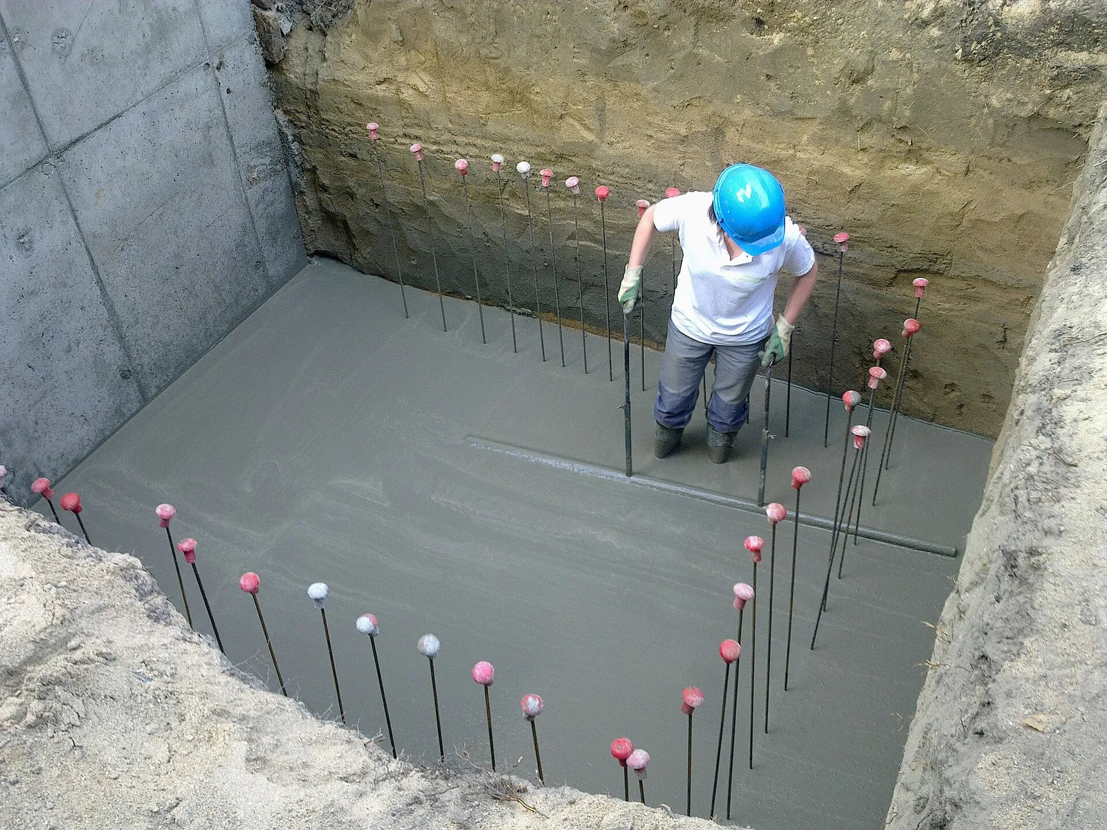 Worker at the bottom of an excavation checking fresh concrete in a raft foundation with projecting reinforcement bars
