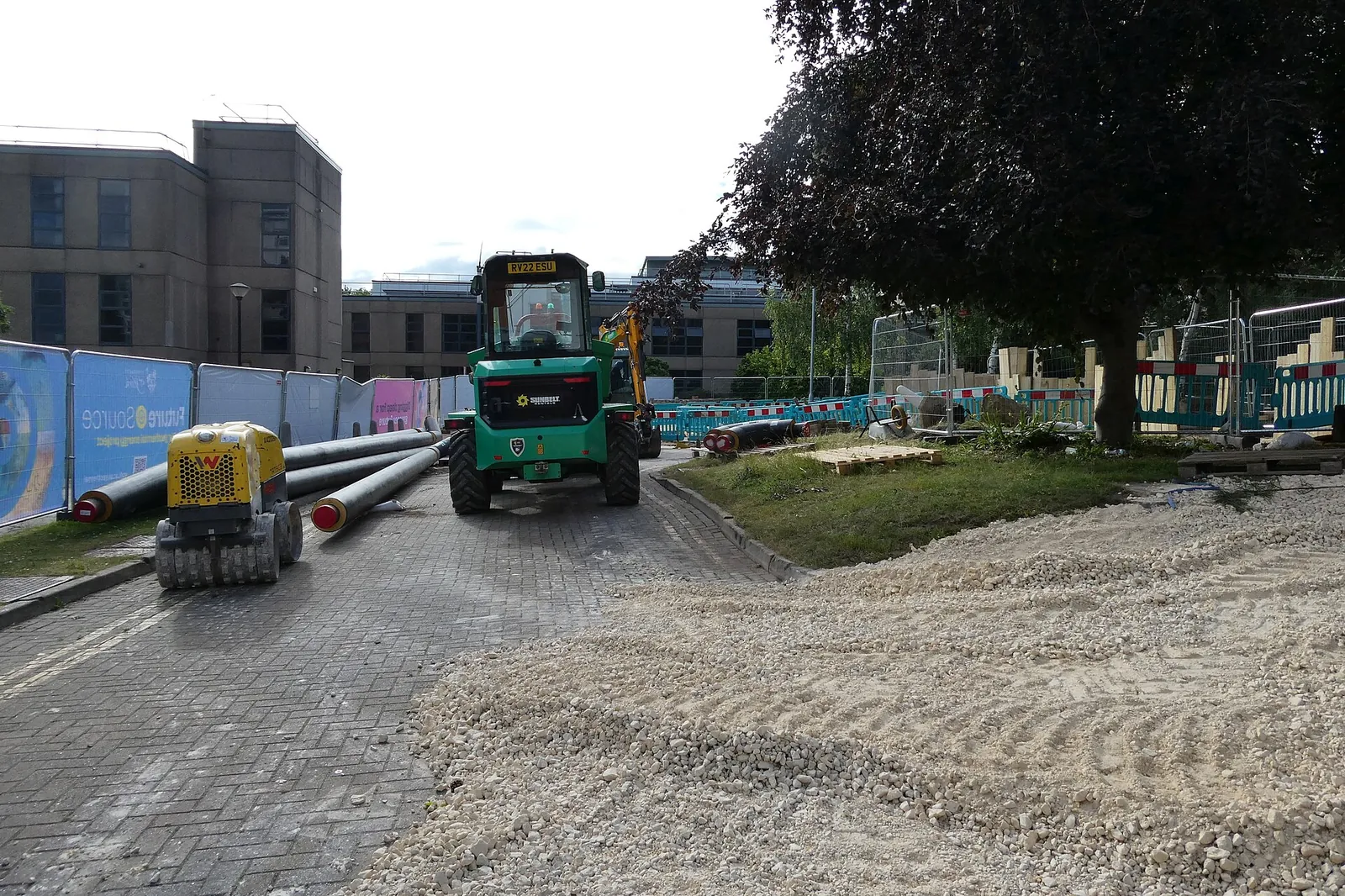 Construction trench with district heating pipes being laid and a green construction vehicle