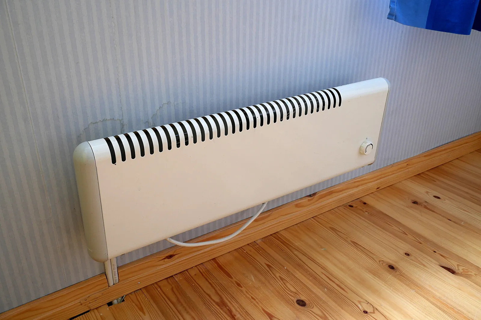 White electric radiator mounted low on a wall above a light wooden floor