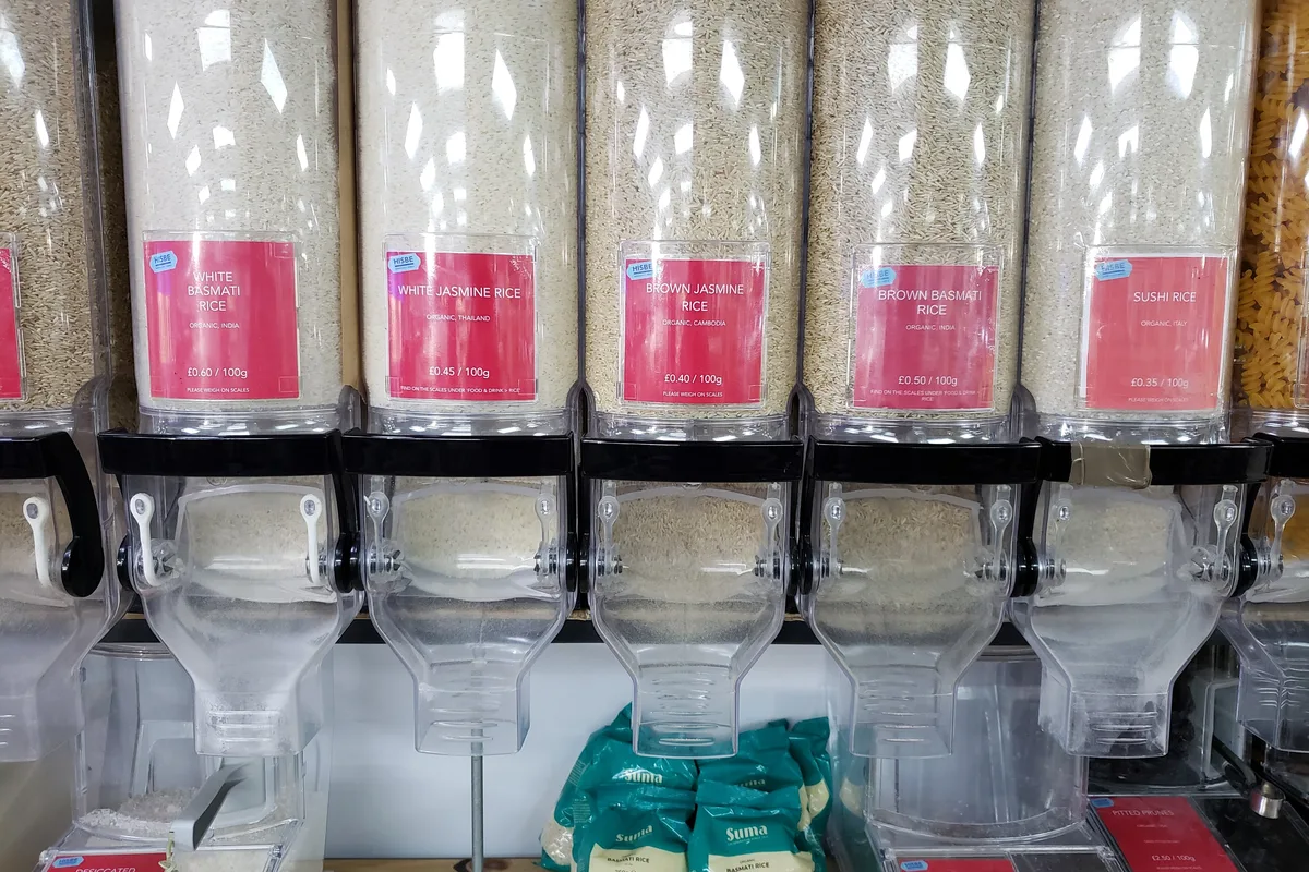 Row of bulk rice dispensers with pink price-per-weight labels, in a package-free grocery shop