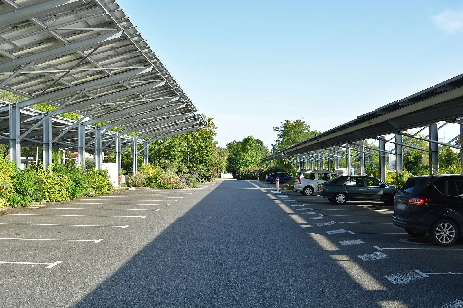 Outdoor car park at an aquatic stadium covered by rows of photovoltaic canopies, with cars parked in the shade