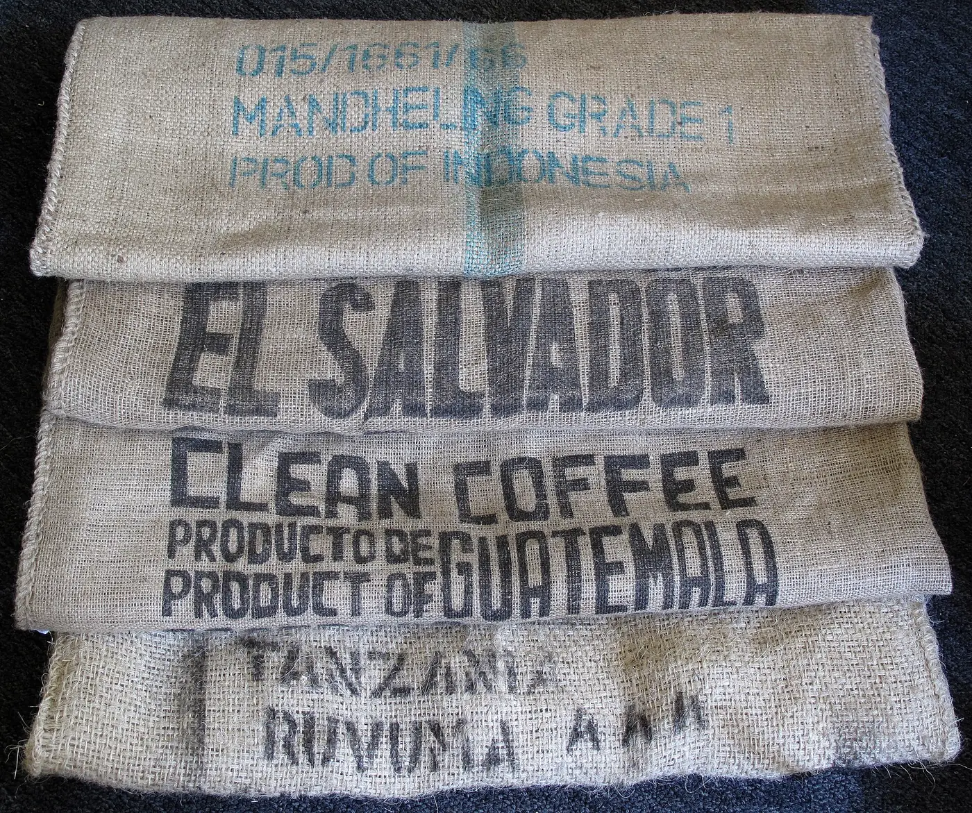 Empty jute coffee sacks, folded and stacked, marked with their origins: Indonesia, El Salvador, Guatemala, Tanzania