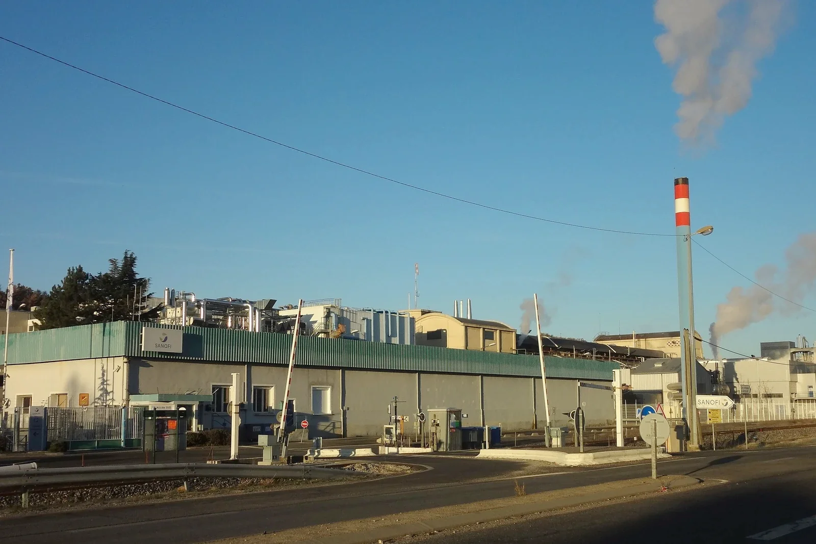 Buildings of the Sanofi plant at Sisteron at sunset, red and white chimney and plumes of steam under a blue sky
